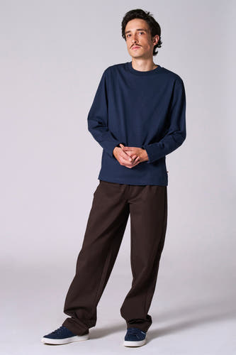T-shirt bleu à manches longues de Le Fabuleux Marcel de Bruxelles, avec un pantalon marron foncé et des baskets bleues.