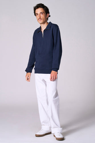 Man met donkerblauwe trui, witte broek en witte sneakers.