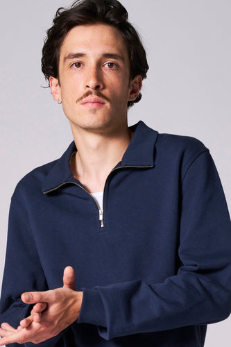 Man met snor in blauwe sweater met rits.
