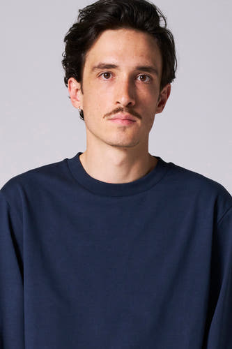 T-shirt bleu à manches longues de Le Fabuleux Marcel de Bruxelles, porté par un modèle avec une barbe et un piercing à l'oreille en argent.