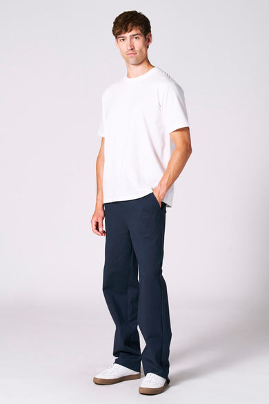T-shirt blanc à manches courtes de Le Fabuleux Marcel de Bruxelles, porté avec un pantalon bleu et des baskets blanches.