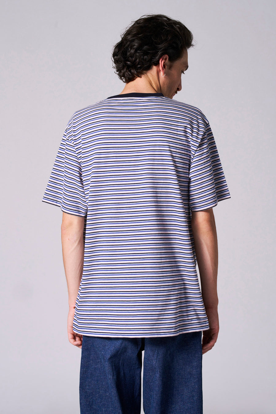 Man met gestreept shirt en blauwe broek, van achteren gezien.