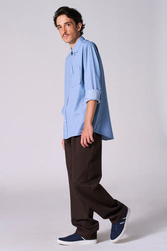 Chemise bleue à manches longues de Le Fabuleux Marcel de Bruxelles, portée avec un pantalon marron et des baskets bleues.