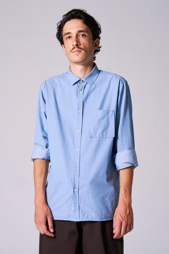 Chemise bleue à manches longues de Le Fabuleux Marcel de Bruxelles, avec des manches retroussées et une poche poitrine.