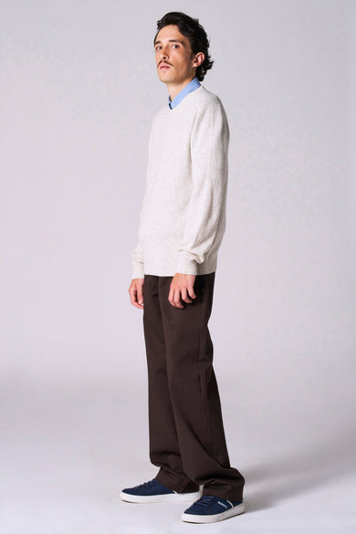 Pull beige à col rond de Le Fabuleux Marcel de Bruxelles, avec des manches longues et porté avec un chemise bleue et un pantalon marron.