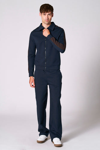 Man in blauwe outfit met bruine accenten, staand.