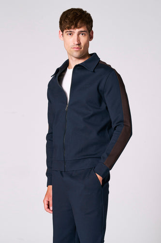 Man in marineblauw joggingpak met bruine accenten tegen witte achtergrond.