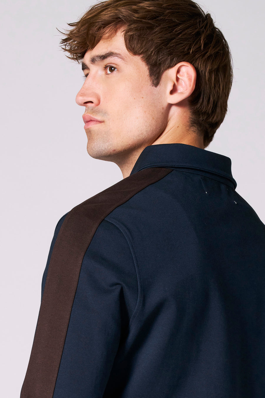 Man met bruin haar, donkerblauw shirt met bruine details, kijkend over zijn schouder.
