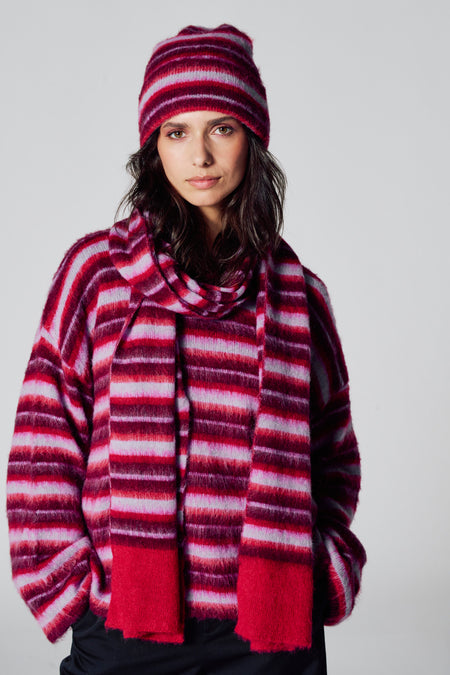 Écharpe d'hiver multicolore de Le Fabuleux Marcel de Bruxelles, avec un motif à rayures, portée avec une casquette et un pull coordonnés.
