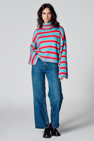 Sweat-shirt multicolore à col montant de Le Fabuleux Marcel de Bruxelles, avec des rayures horizontales et porté avec des jeans bleus et des chaussures noires.