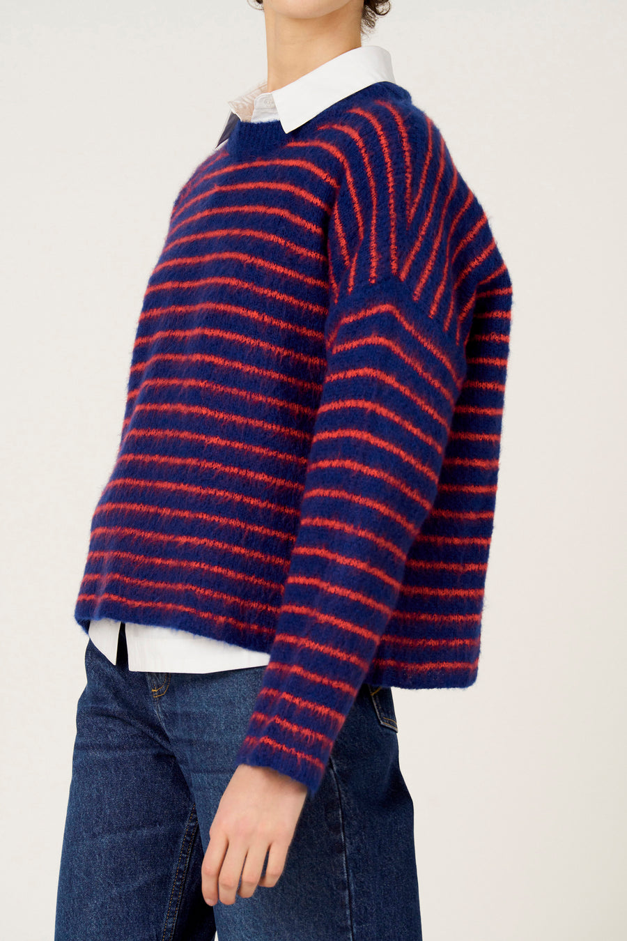 Pull multicolore à col rond de Le Fabuleux Marcel de Bruxelles, avec des rayures rouges, combiné avec une chemise blanche et un jean bleu.