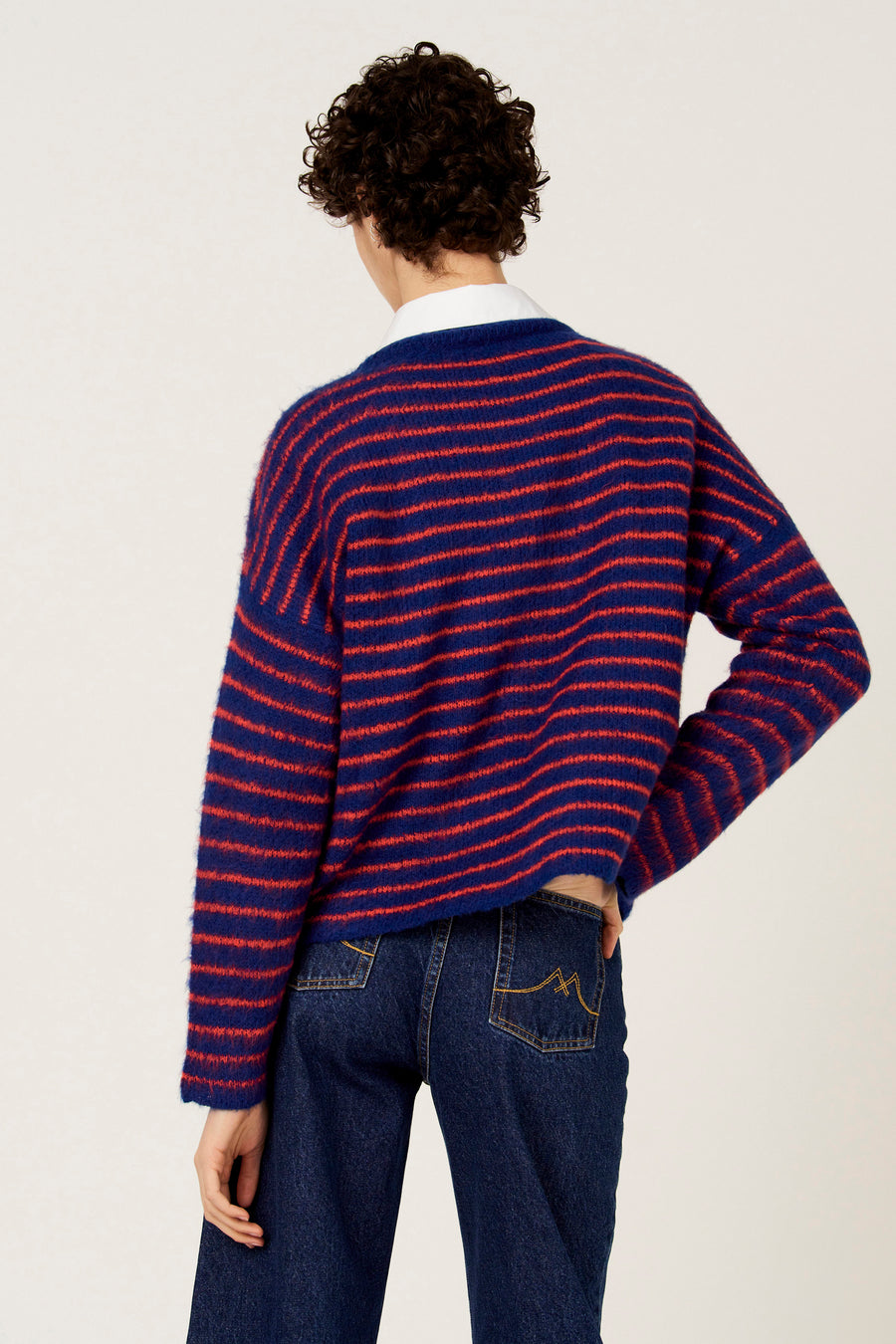 Pull multicolore à col rond de Le Fabuleux Marcel de Bruxelles, avec des rayures horizontales et porté avec un jean foncé.