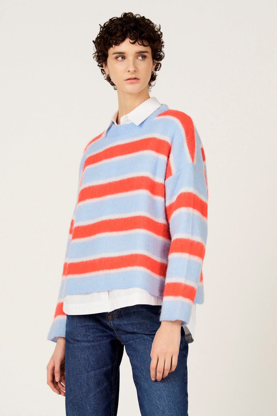 Multikleurige trui met ronde hals van Le Fabuleux Marcel de Bruxelles, met gestreept patroon en gedragen over een wit overhemd met jeans.
