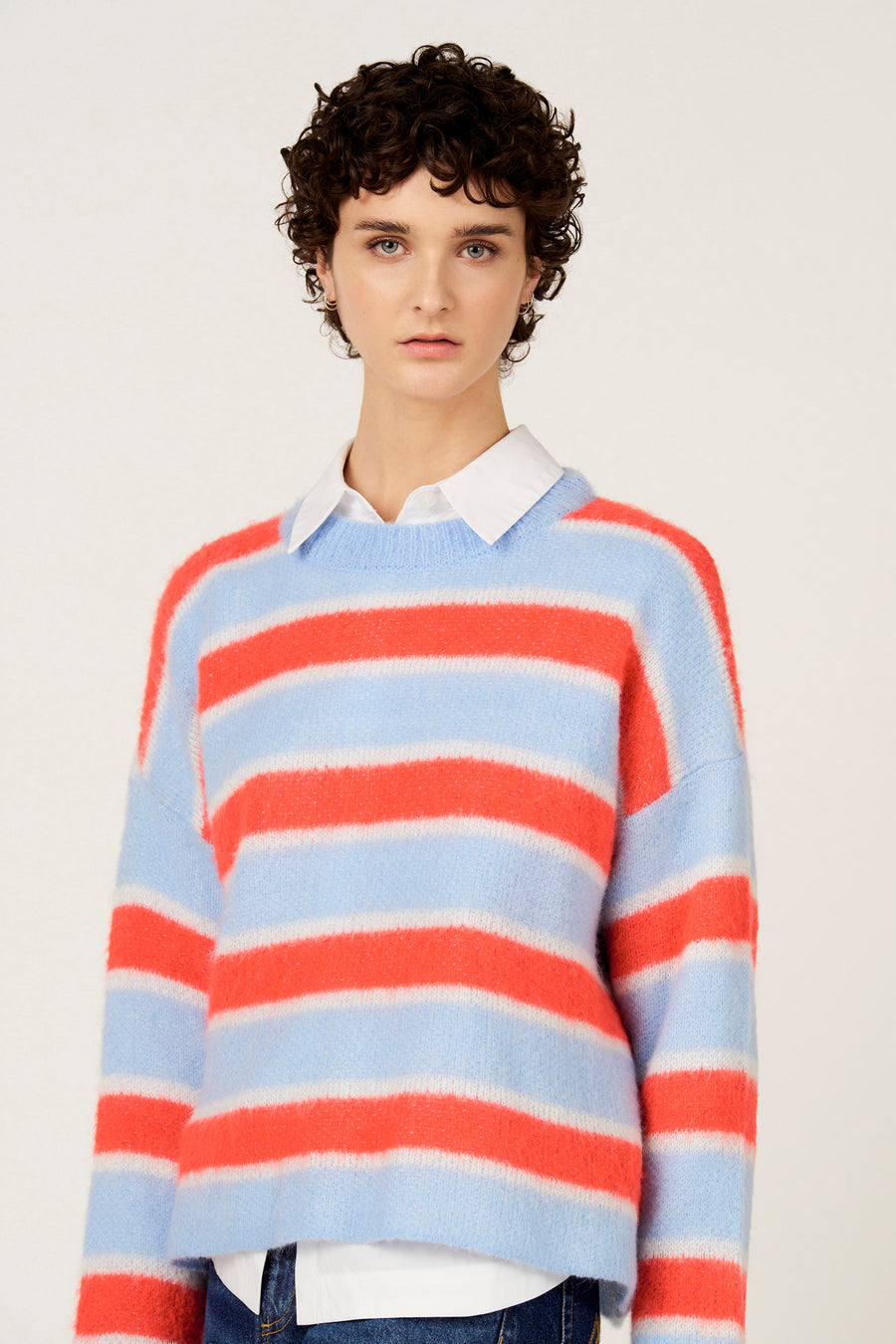 Pull multicolore à col rond de Le Fabuleux Marcel de Bruxelles, avec des rayures horizontales et porté sur une chemise blanche.