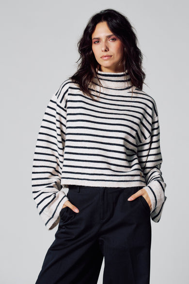 Manteau multicolore de Le Fabuleux Marcel de Bruxelles, motif rayé, longues manches et porté avec un pantalon noir.