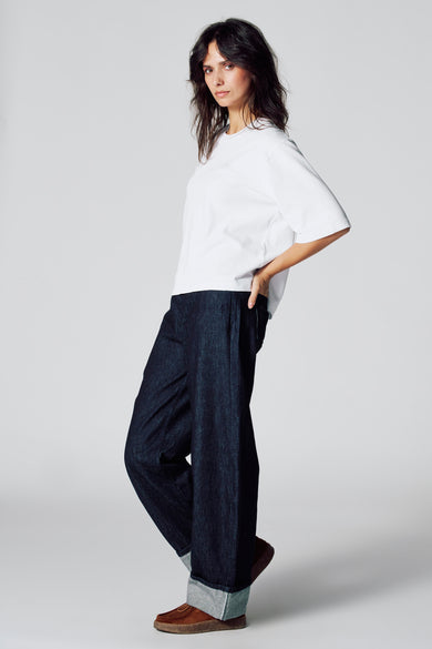 T-shirt blanc à manches courtes de Le Fabuleux Marcel de Bruxelles, porté avec des jeans larges et sombres et des chaussures marrons.