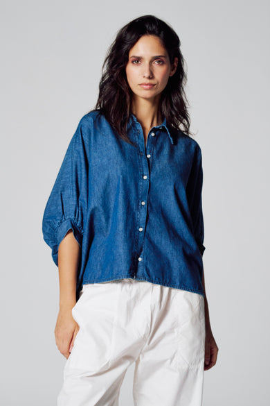Chemise de denim bleu marine à manches courtes de Le Fabuleux Marcel de Bruxelles, vue arrière, associée à un pantalon blanc.