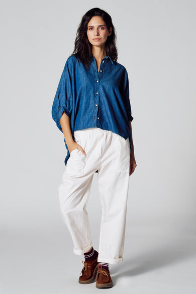 Chemise de denim bleu marine à manches courtes de Le Fabuleux Marcel de Bruxelles, portée avec un short blanc et des chaussures marrons.