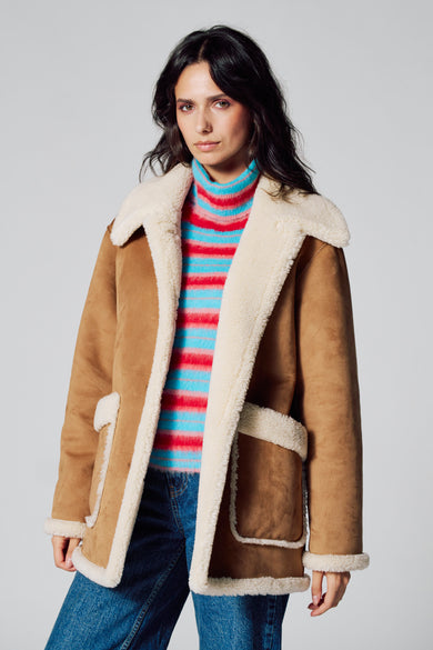 Manteau long brun de Le Fabuleux Marcel de Bruxelles, avec une doublure blanche et un pull rayé et des jeans bleus.