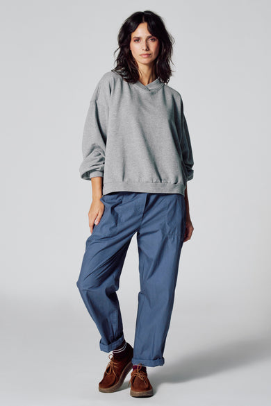 Pull gris de Le Fabuleux Marcel de Bruxelles, avec des manches longues, associé à un pantalon bleu et des chaussures marrons.