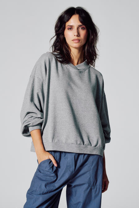 Pull gris de Le Fabuleux Marcel de Bruxelles, avec des manches longues et associé à un pantalon bleu.