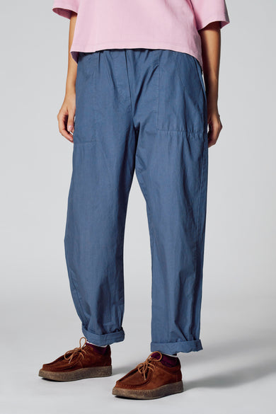 Pantalon bleu 7/8 de Le Fabuleux Marcel de Bruxelles, avec des poches pliées et des chaussures marrons.