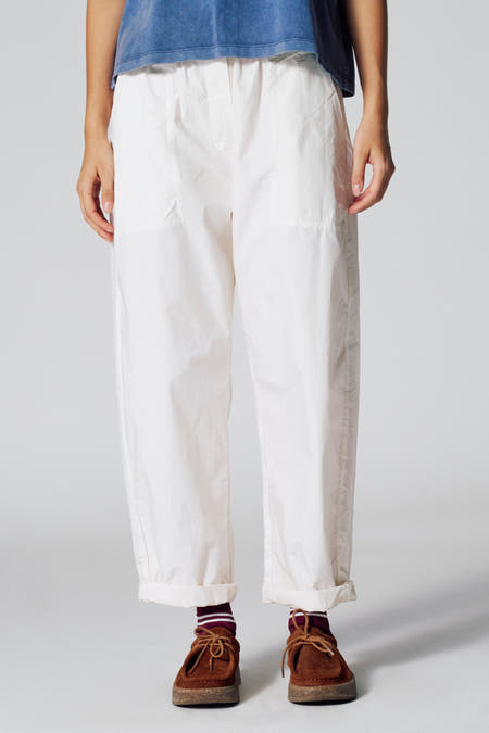 Pantalon 7/8 blanc de Le Fabuleux Marcel de Bruxelles, avec des jambes de pantalon repliées, associé à des chaussettes rayées et des chaussures brunes.
