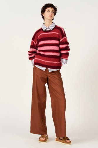 Pull multicolore à col rond de Le Fabuleux Marcel de Bruxelles, avec des rayures horizontales et porté avec une chemise rayée et un pantalon marron.