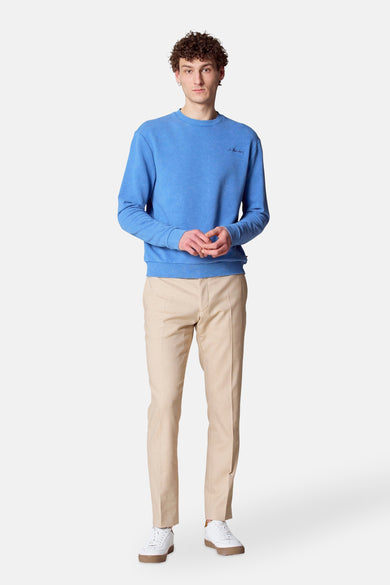 Pull-over bleu avec col rond de Le Fabuleux Marcel de Bruxelles, porté avec un pantalon beige et des baskets blanches.