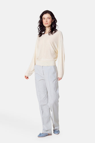 Vrouw draagt beige trui en gestreepte broek.