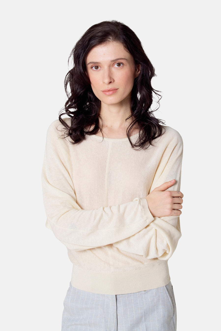 Vrouw in roomkleurige trui en gestreepte broek, armen gekruist.
