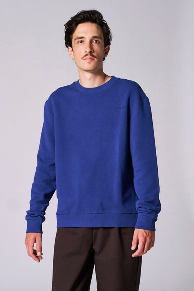 Pull bleu de Le Fabuleux Marcel de Bruxelles, à longues manches, associé à un pantalon marron.