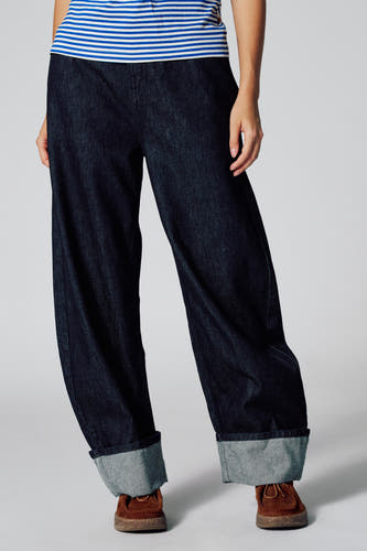Jean bleu marine denim LE JEAN BALLOON de Le Fabuleux Marcel de Bruxelles, avec des poches de pantalon rabattues et des chaussures marron.