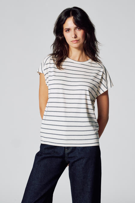 T-shirt beige à manches courtes de Le Fabuleux Marcel de Bruxelles, avec des rayures bleu marine horizontales, porté avec un jeans bleu marine.