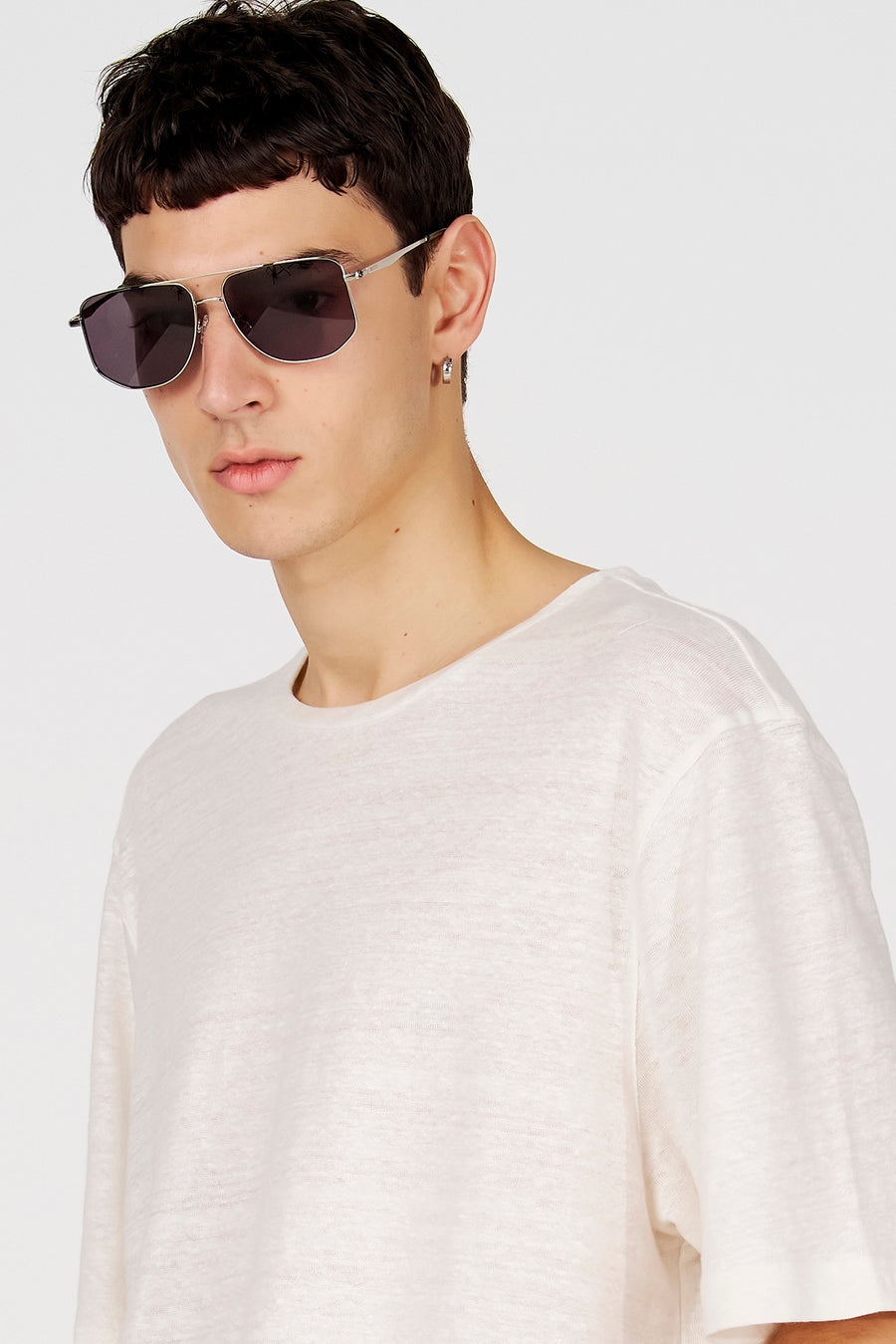Lunettes de soleil bleues de Le Fabuleux Marcel de Bruxelles, avec une monture en métal et portées par un homme avec un t-shirt blanc et une boucle d'oreille argentée.