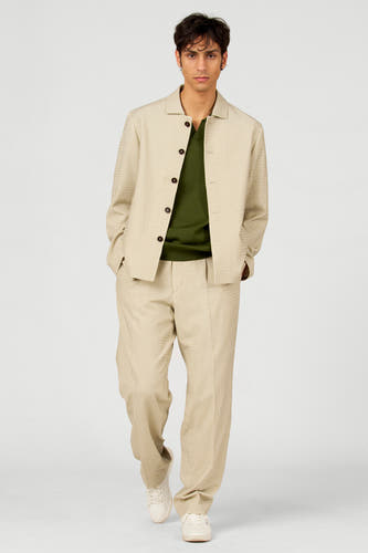 Polo verte de Le Fabuleux Marcel de Bruxelles, portée sous un costume beige à boutons.
