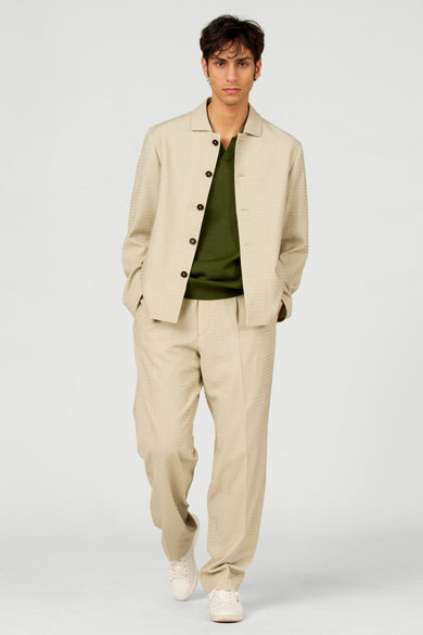 Polo verte de Le Fabuleux Marcel de Bruxelles, portée sous un costume beige à boutons.