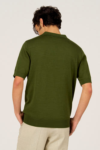 Polo verte de Le Fabuleux Marcel de Bruxelles, à manches courtes et portée avec un pantalon rayé.