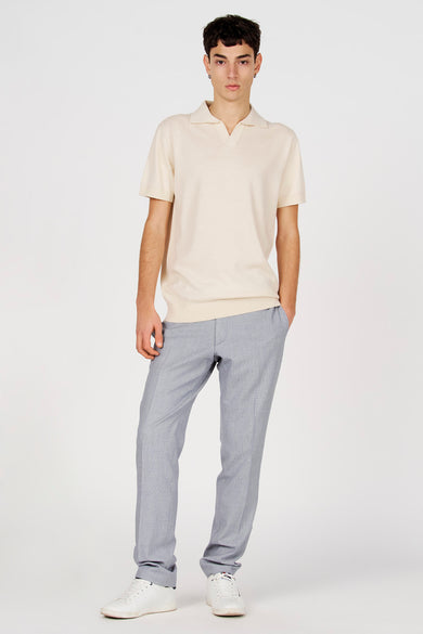 Polo blanche de Le Fabuleux Marcel de Bruxelles, à manches courtes, portée avec un pantalon gris et des baskets blanches.