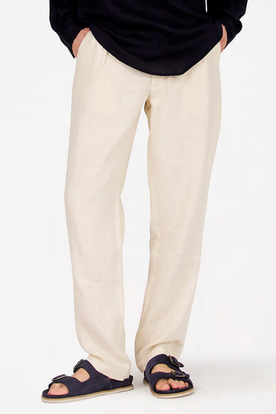 Pantalon de costume écru de Le Fabuleux Marcel de Bruxelles, avec une texture légère et porté avec des sandales bleues.