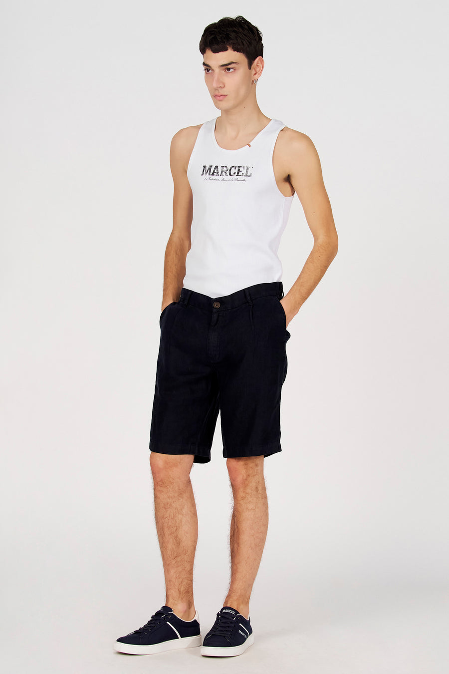 Bermuda bleu de Le Fabuleux Marcel de Bruxelles, porté avec un t-shirt blanc et des baskets bleues.