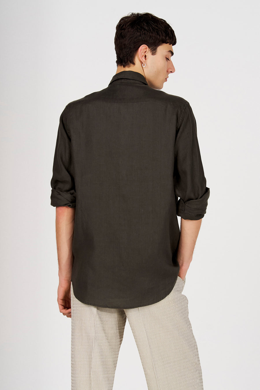 Chemise verte de Le Fabuleux Marcel de Bruxelles avec manches retroussées, vue de dos, stylée avec un pantalon rayé et une boucle d'oreille.