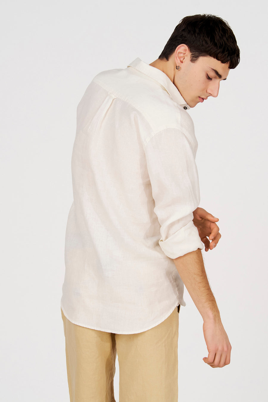 Chemise blanche en lin à manches longues de Le Fabuleux Marcel de Bruxelles, stylée de manière décontractée avec des manches retroussées et un pantalon beige.
