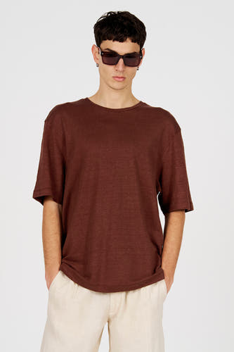 T-shirt marron à manches courtes de Le Fabuleux Marcel de Bruxelles, avec une coupe ample et porté avec un pantalon de couleur crème et des lunettes de soleil foncées.