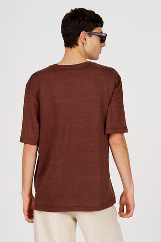 T-shirt marron à manches courtes de Le Fabuleux Marcel de Bruxelles, vu de dos, combiné avec un pantalon de couleur crème et une boucle d'oreille argentée.