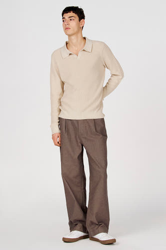 Polo blanche à manches longues et à texture côtelée de Le Fabuleux Marcel de Bruxelles, associée à un pantalon marron ample et des baskets blanches.