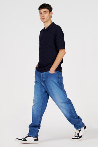 Pull bleu col en V de Le Fabuleux Marcel de Bruxelles, avec un motif texturé subtil, porté avec un jean et des baskets.