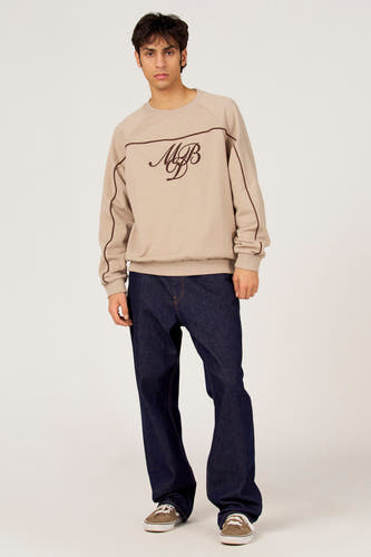Pull gris à col rond de Le Fabuleux Marcel de Bruxelles, avec un logo marron et des accents marron sur les épaules, combiné avec un jean foncé et des baskets marron.