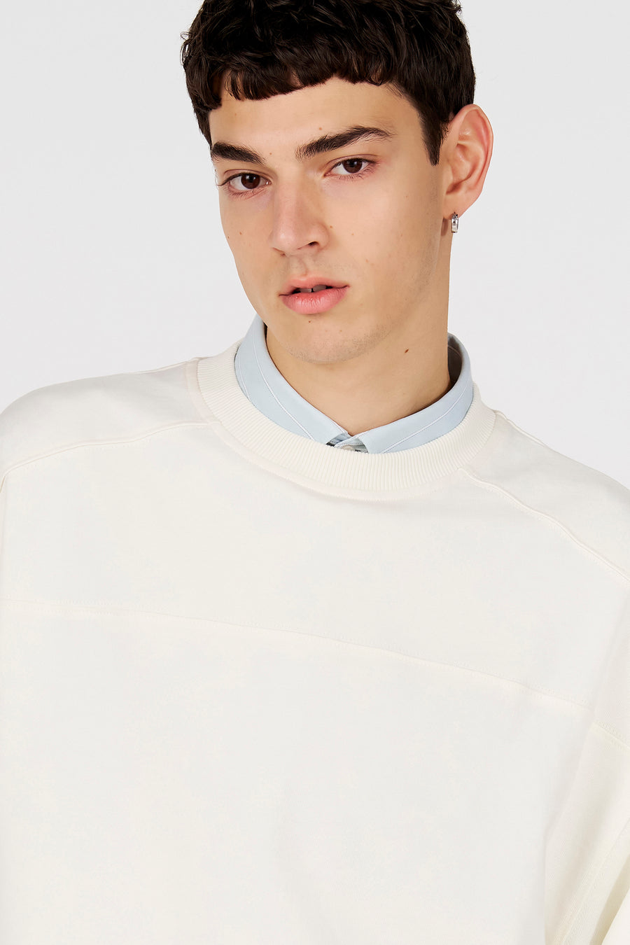 Pull blanc de Le Fabuleux Marcel de Bruxelles, avec une bande horizontale subtile sur la poitrine et une chemise bleu clair en dessous.