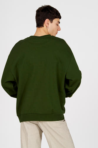 Pull vert à col rond de Le Fabuleux Marcel de Bruxelles, vue arrière, porté avec un pantalon rayé.